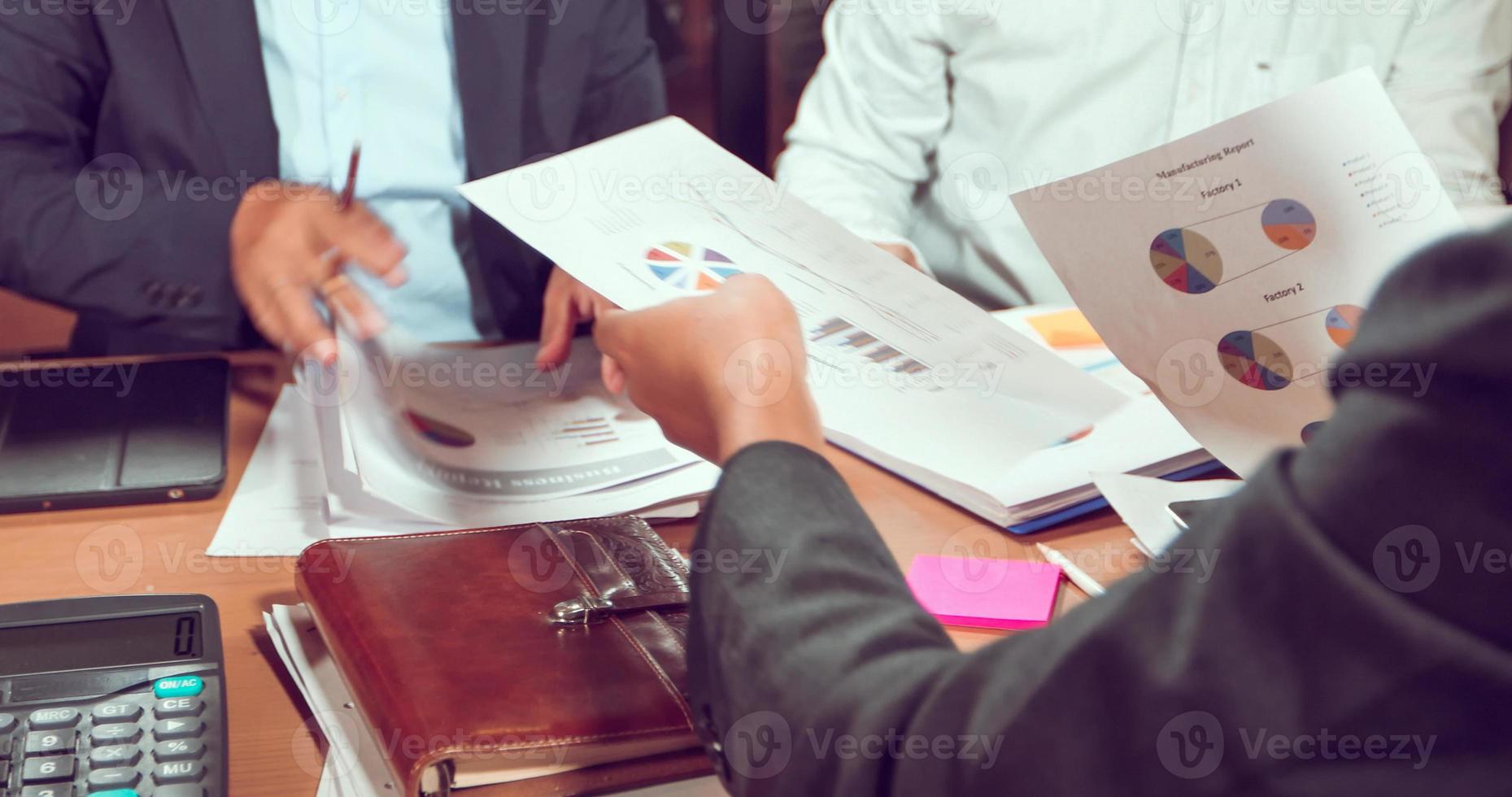 Asian businessmen and businesswomen analysis documents on office table with laptop computer and graph financial diagram working in the background photo
