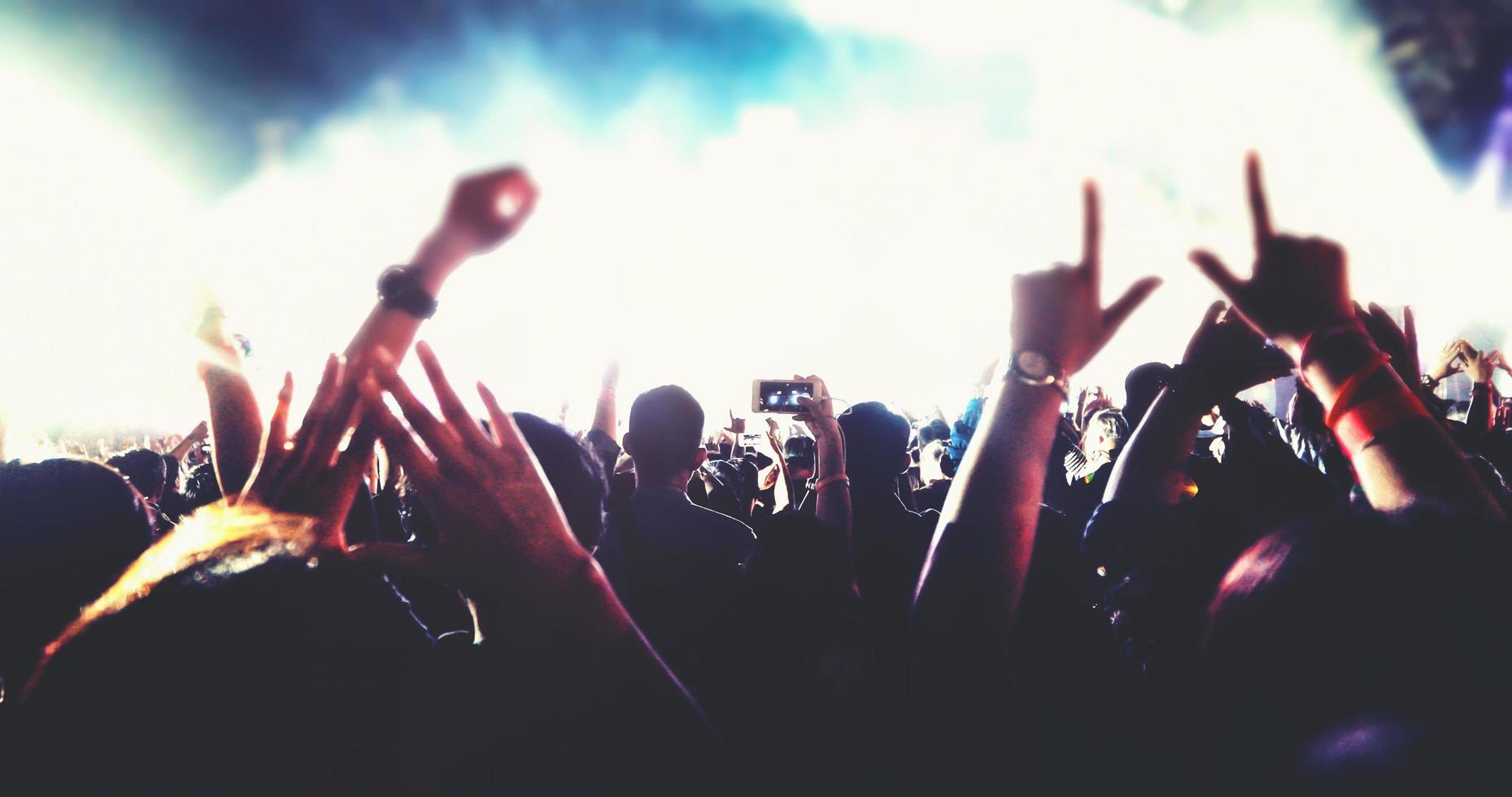 siluetas borrosas de la multitud de conciertos en la vista trasera de la multitud del festival levantando las manos en las luces brillantes del escenario foto