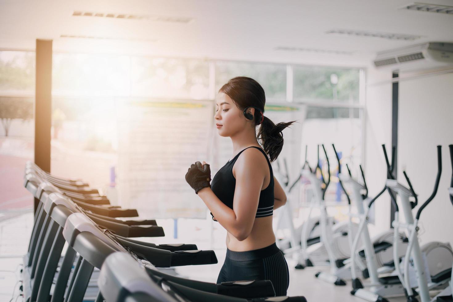 Las mujeres asiáticas corriendo zapatos deportivos en el gimnasio, mientras que una joven mujer caucásica está haciendo jogging en la cinta de correr foto