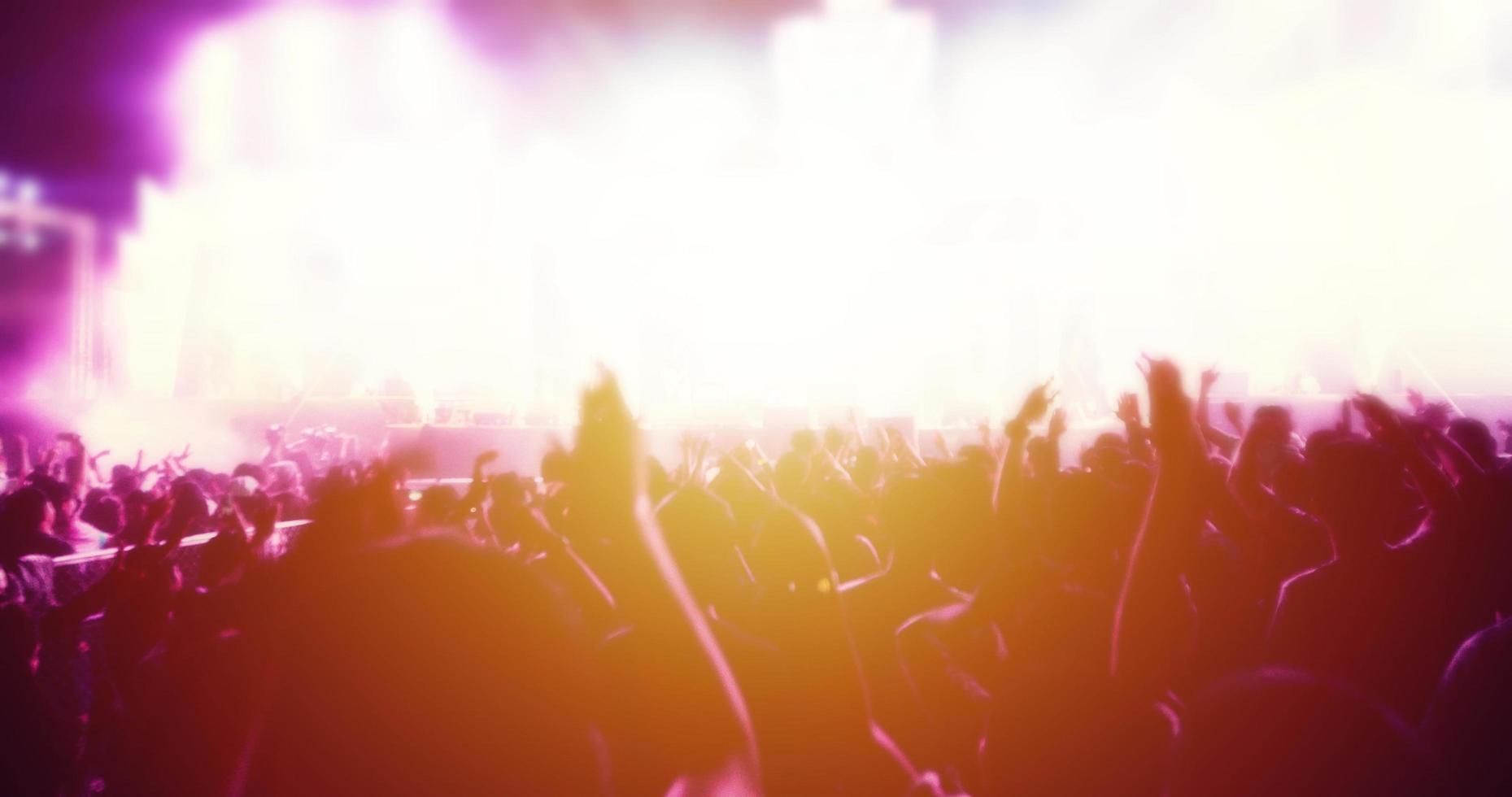 silhouettes of concert crowd at Rear view of festival crowd raising their hands on bright stage lights photo