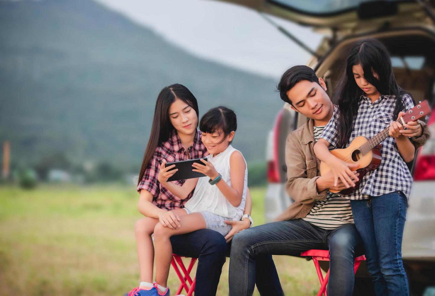 Niña feliz tocando el ukelele con la familia asiática sentada en el coche para disfrutar del viaje por carretera y las vacaciones de verano foto