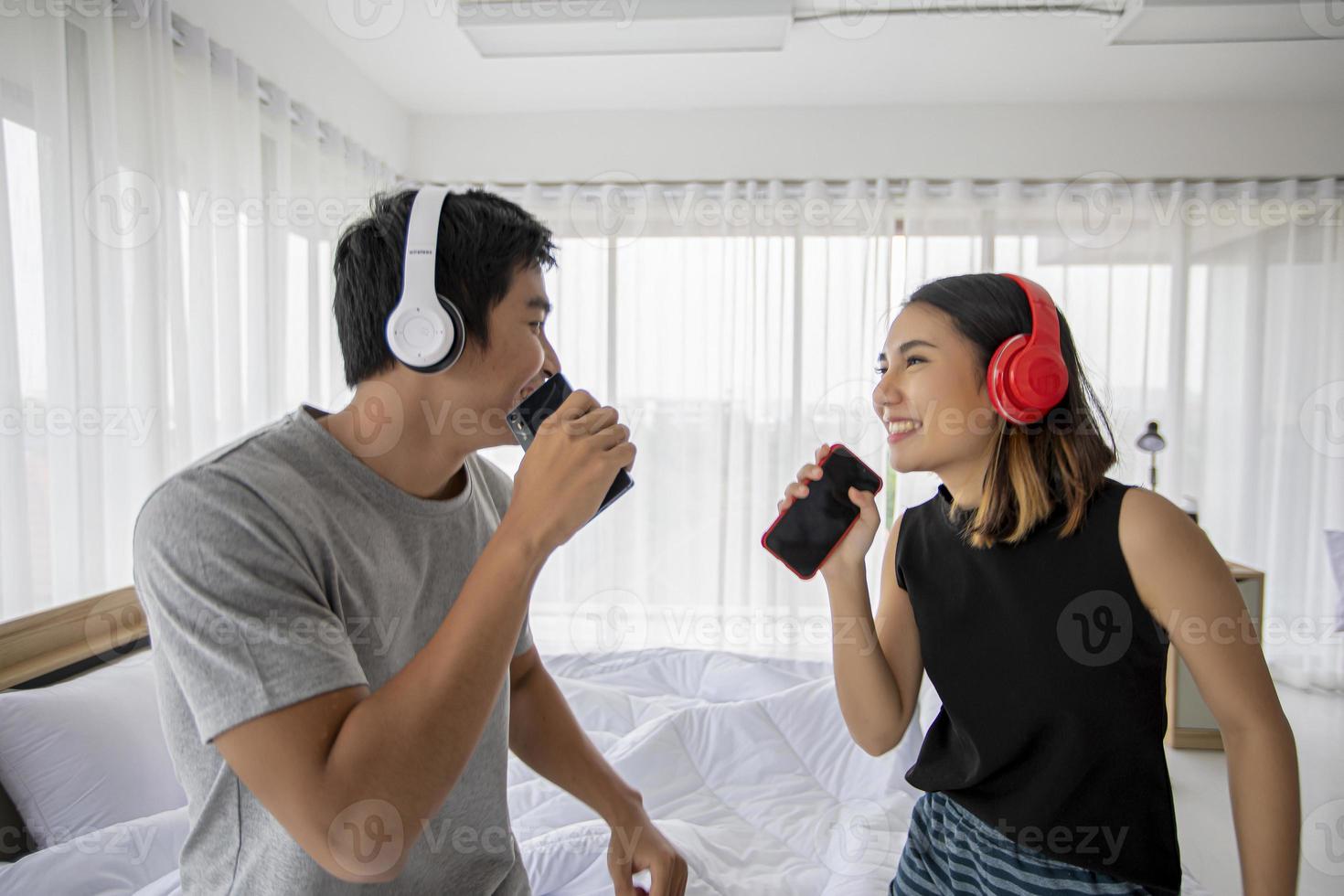 amantes de la pareja asiática escuchando música y cantando en su dormitorio y felices en el tiempo de relajación foto