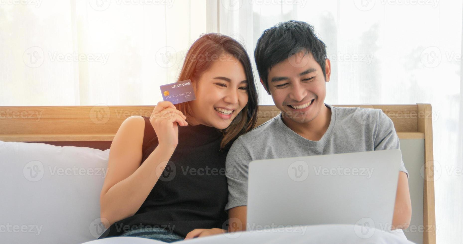 Asian Couple shopping online and paying with credit card at laptop computer,Happy couple at home surfing the net in bed photo