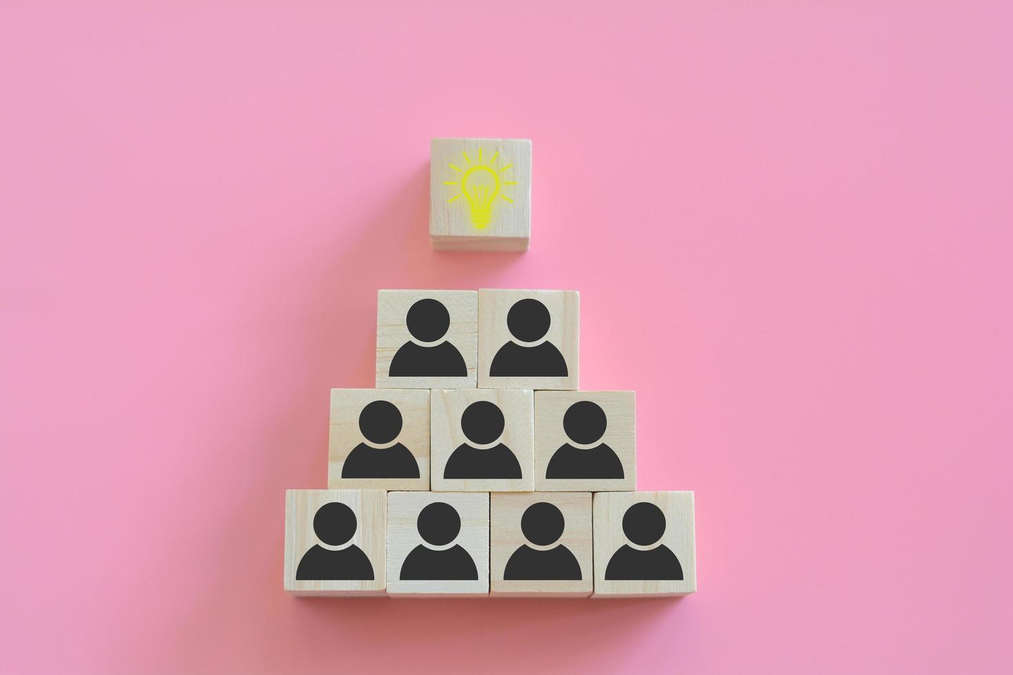 Teamwork and creative thinking and innovation concept. The pyramids of wooden blocks with human icons and bright light bulbs on a pink background. Collaboration of people in the organization. photo