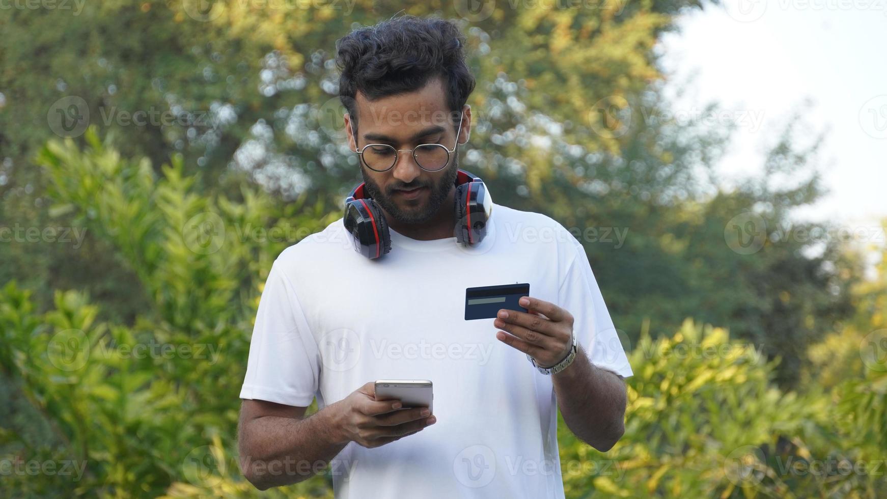 Cheerful young Man guy in casual shirt, White t-shirt posing isolated on Beautiful background. People lifestyle concept. Using mobile phone hold credit bank card photo