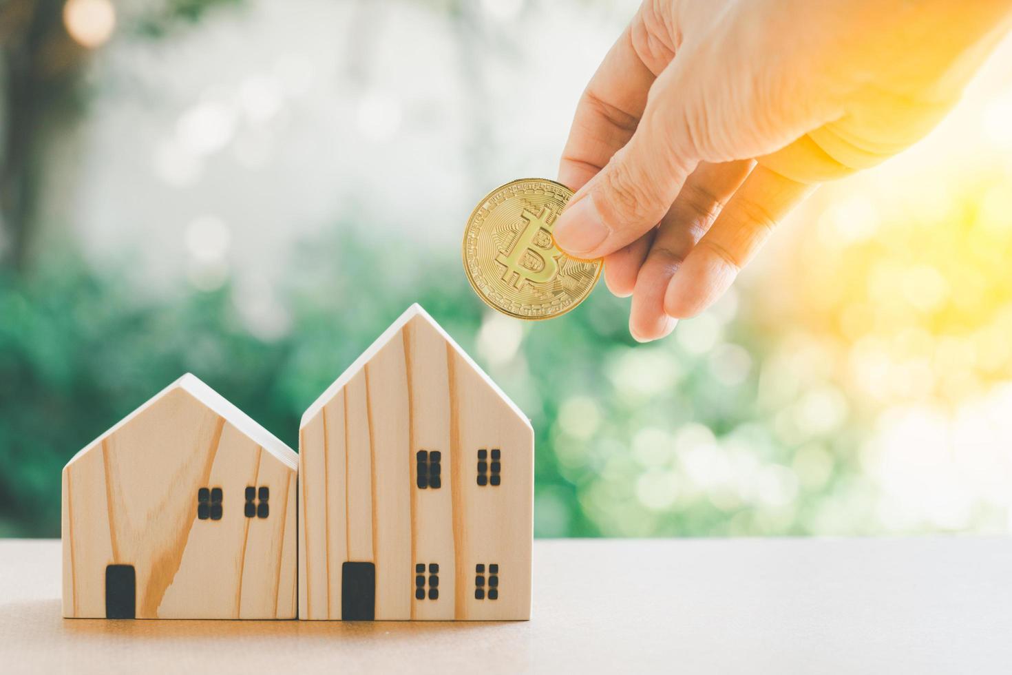 Saving money concept. Hand hold gloden coin with wooden model home on table with green bokeh background. Saving or investment for home in the future. photo