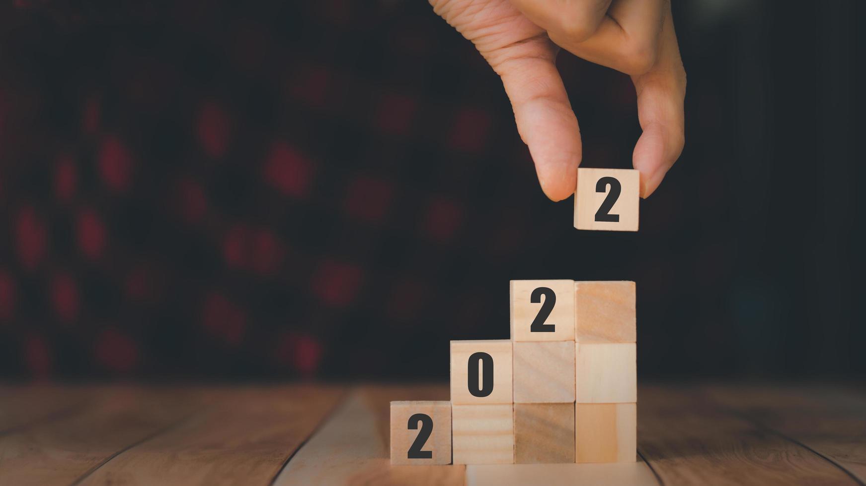 2022 New year concept. Businessman holding wooden cube block of number 2 and place on the column on wooden table. photo