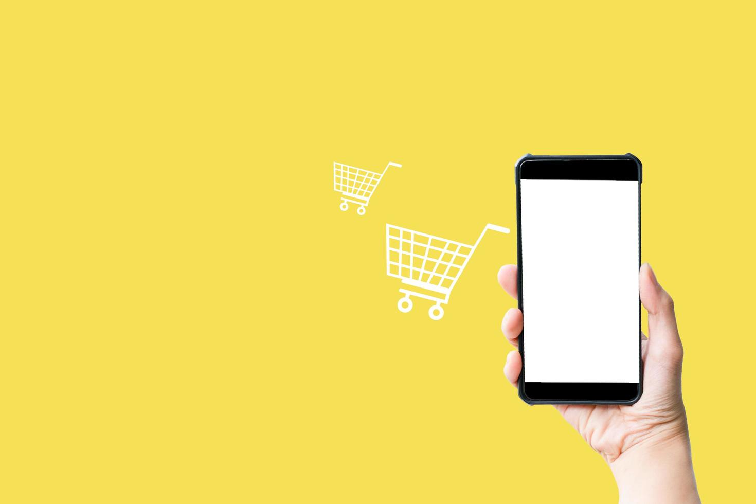 Shop online concept. Hand hold smartphone with shopping cart virtual icon on yellow background. Quarantine to save life from corona virus. photo