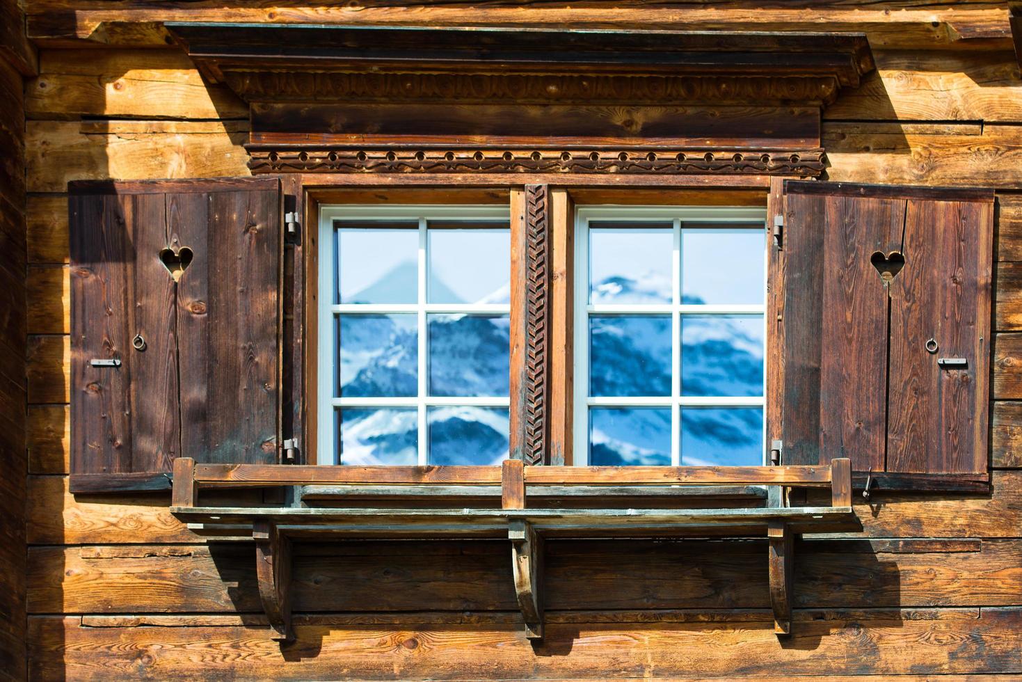 Typical wooden house window in the mountains with mirrored mountains photo