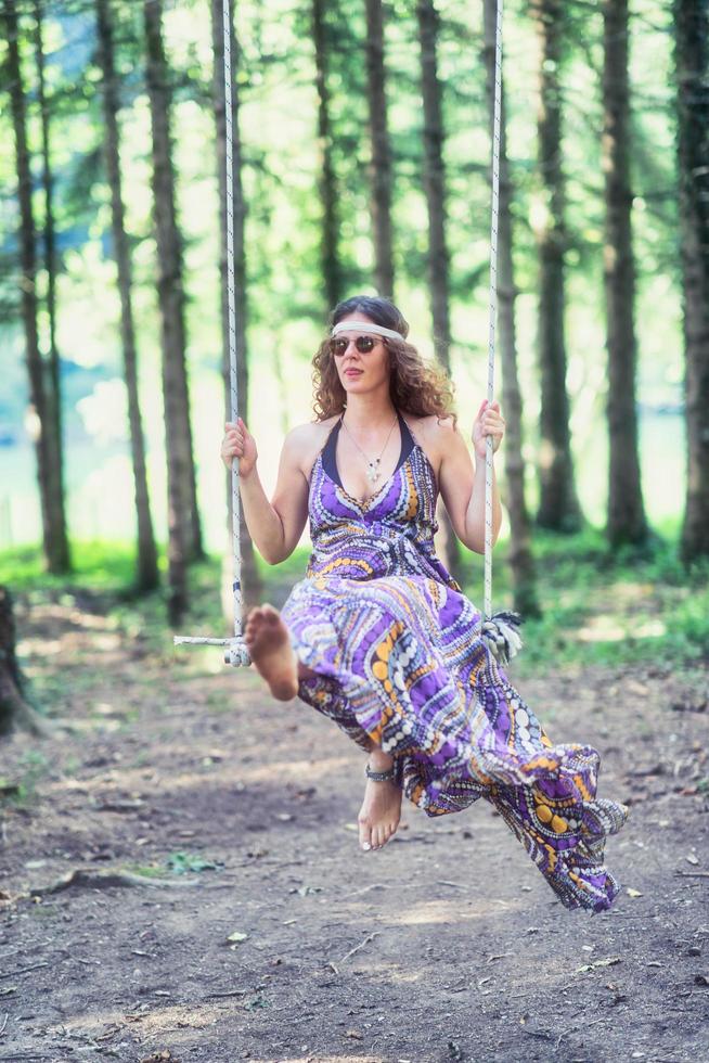 Hippie style girl swings on swing in the woods photo