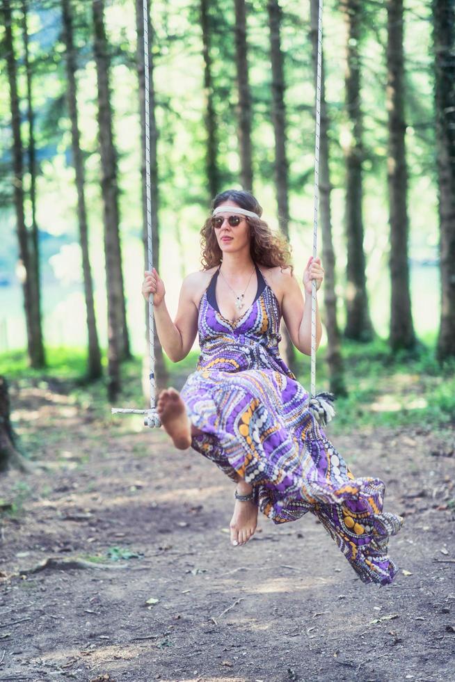 chica de estilo hippie columpios en columpio en el bosque foto