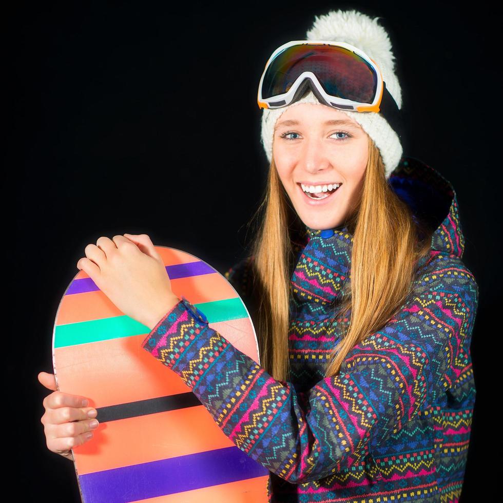 niña sonriente con ropa de esquí con snowboard sobre fondo negro en el estudio foto