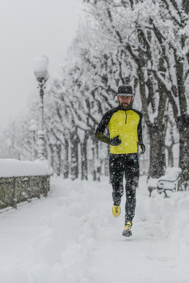 Athlete man runs on a city sidewalk during heavy snowfall photo