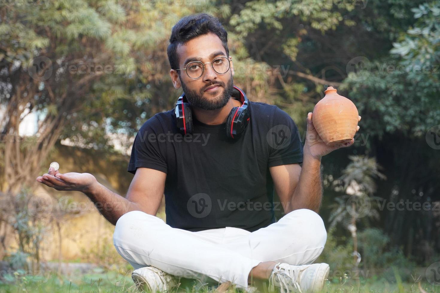 A man holds an earphone on his shoulder and deposit the money on his piggy bank photo