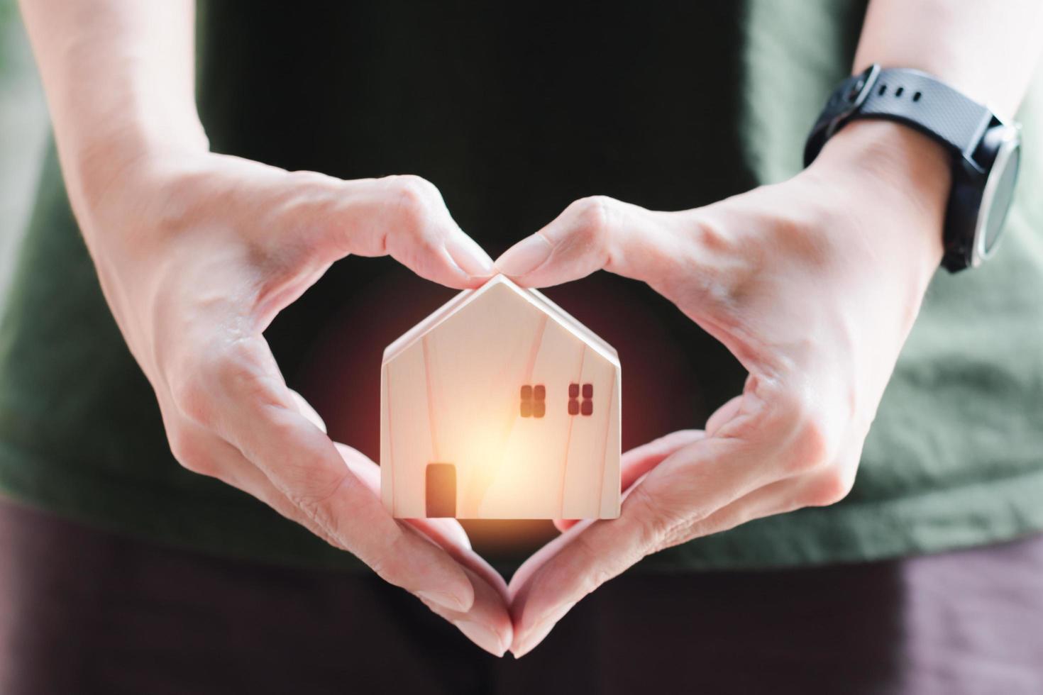 Home sweet home. Wooden home in blurry heart shape hand holding . Small house with love. photo