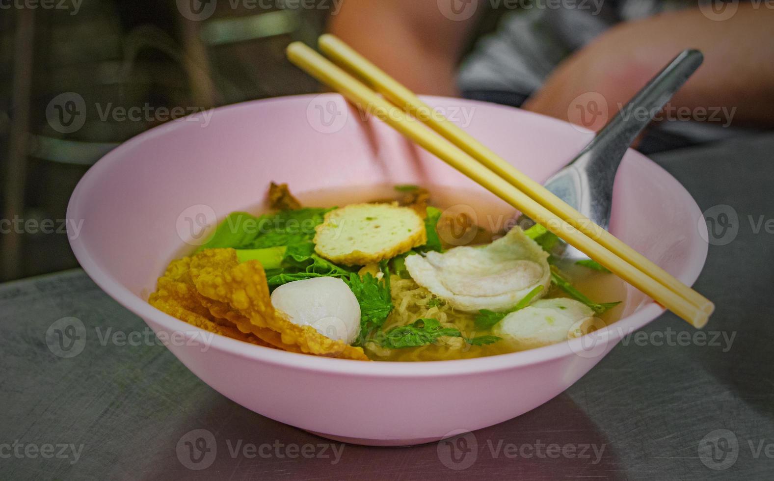 sopa de fideos tailandesa con bolas de pescado palillos de tazón rosa tailandia. foto