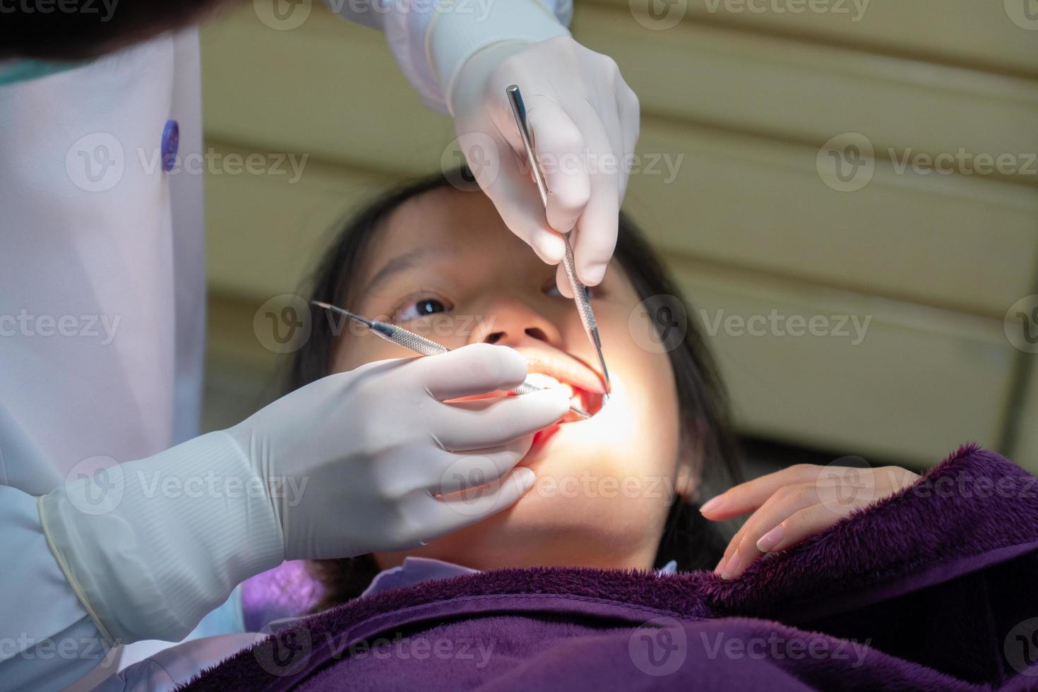 joven dentista y asistente dental haciendo un procedimiento para tratar la caries dental para una niña en la clínica foto