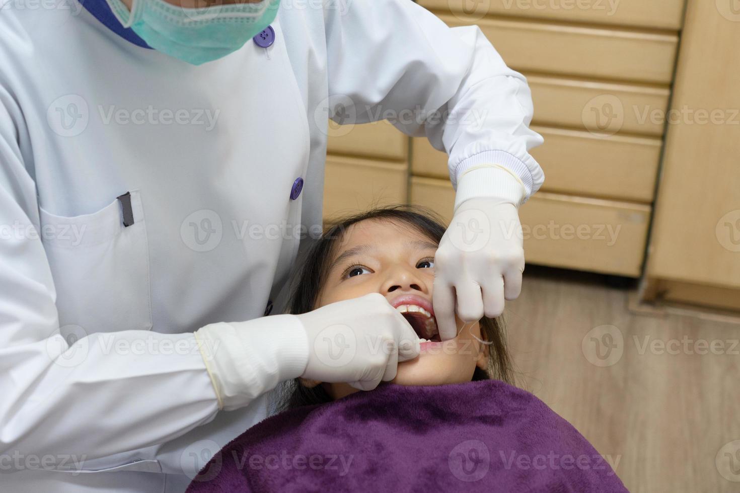 dentista que usa fross dental para limpiar el diente de una niña en la clínica foto