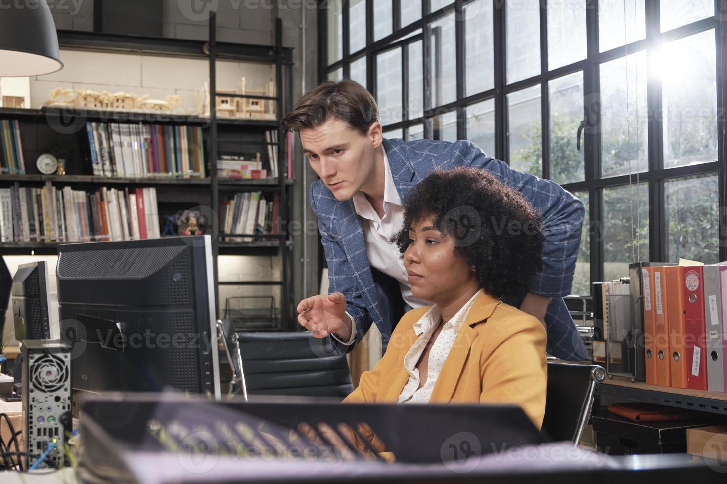 la joven trabajadora afroamericana se sienta, trabaja con la computadora, hace una lluvia de ideas, habla y discute con un colega caucásico y una sociedad sobre trabajos comerciales en la empresa de oficinas del espacio de trabajo. foto