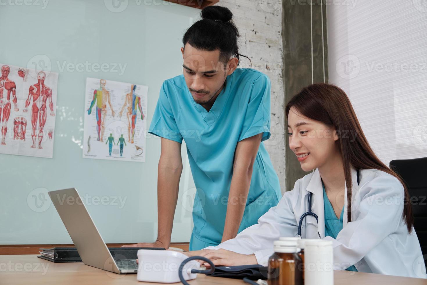 Healthcare team partners. Two uniformed young Asian ethnicity doctors are co-workers discussing medication in hospital's clinic office. Specialist persons are experts and professionals. photo