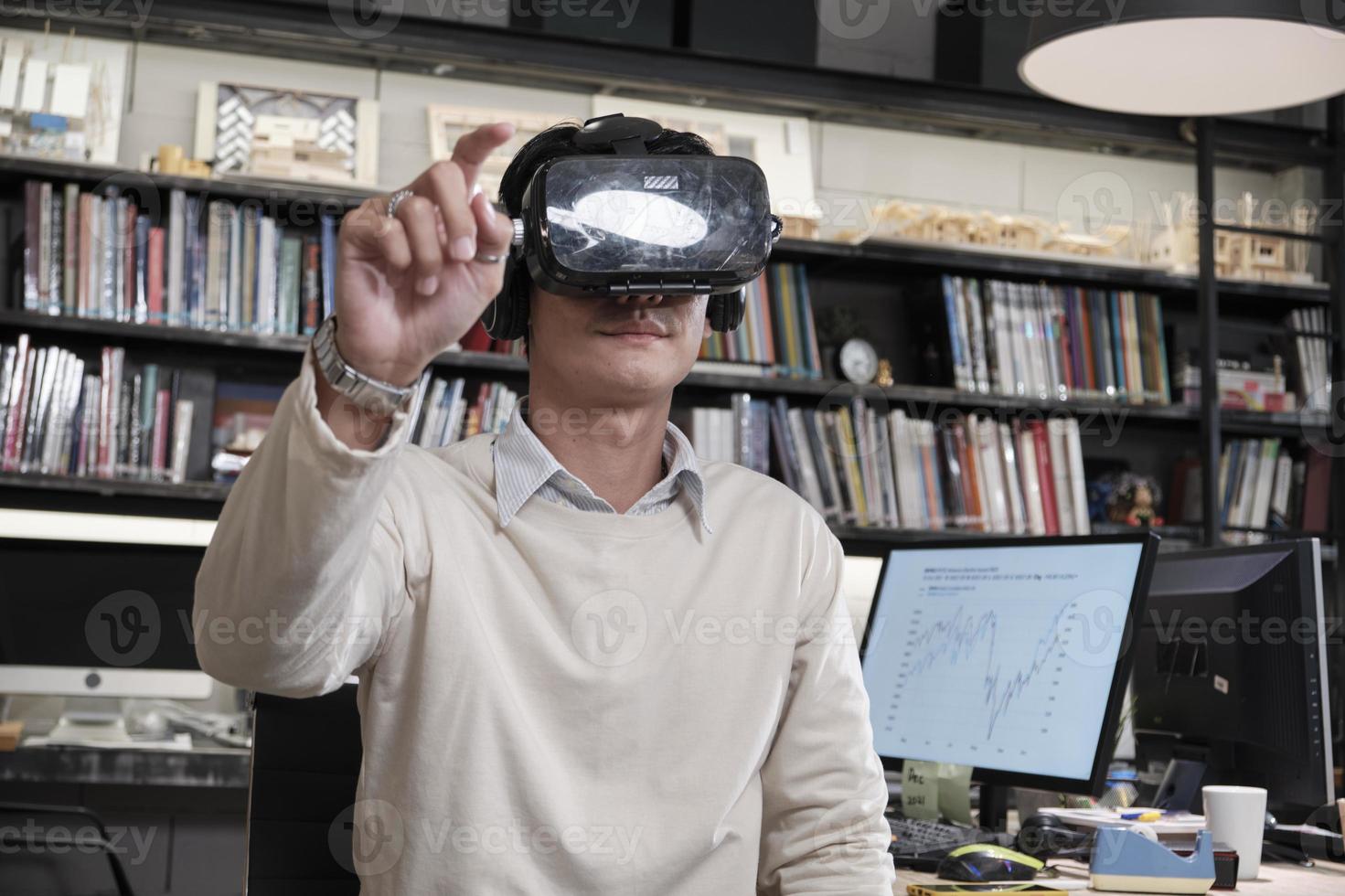 Asian male worker use VR headset simulator equipment to visualization 3D cyberspace, view and interactive touch, futuristic digital workspace at business office, gadget device, exciting experience. photo