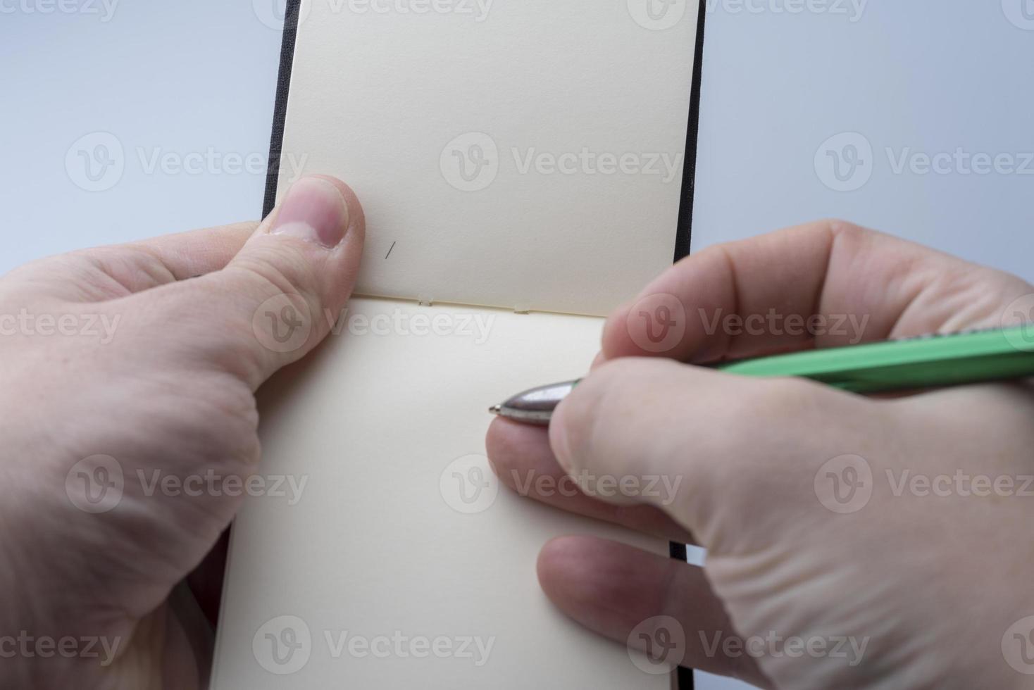 manos de un hombre que sostiene un cuaderno y un bolígrafo sobre un fondo blanco. foto