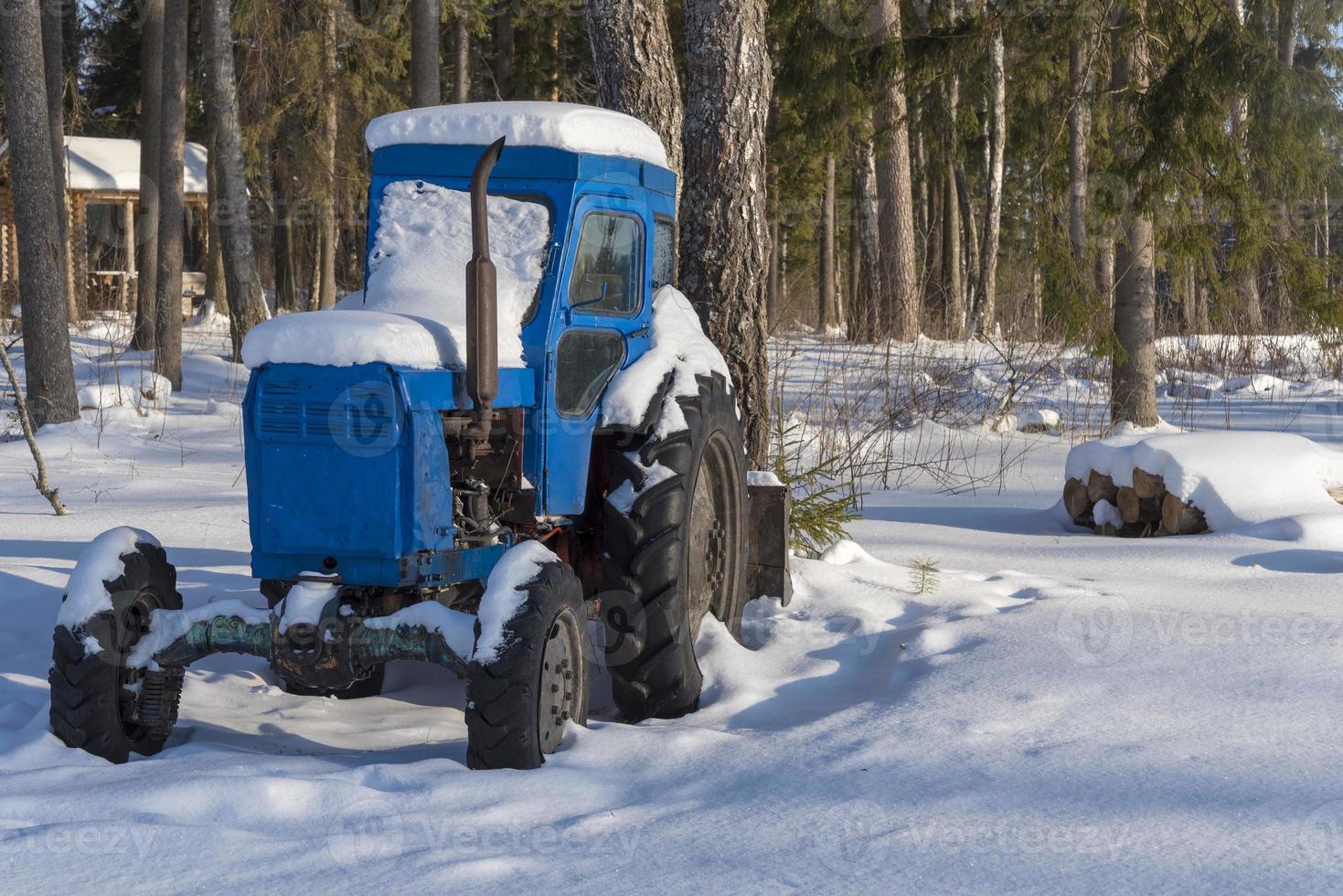 tractor cubierto de nieve en el bosque cerca del pueblo. foto