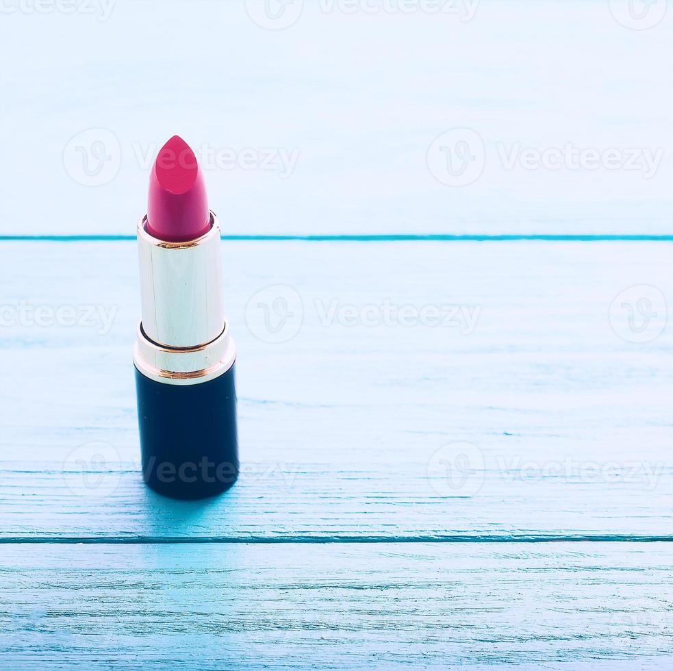 Pink lipstick in focus on blue wooden background. Selective focus and copy space photo