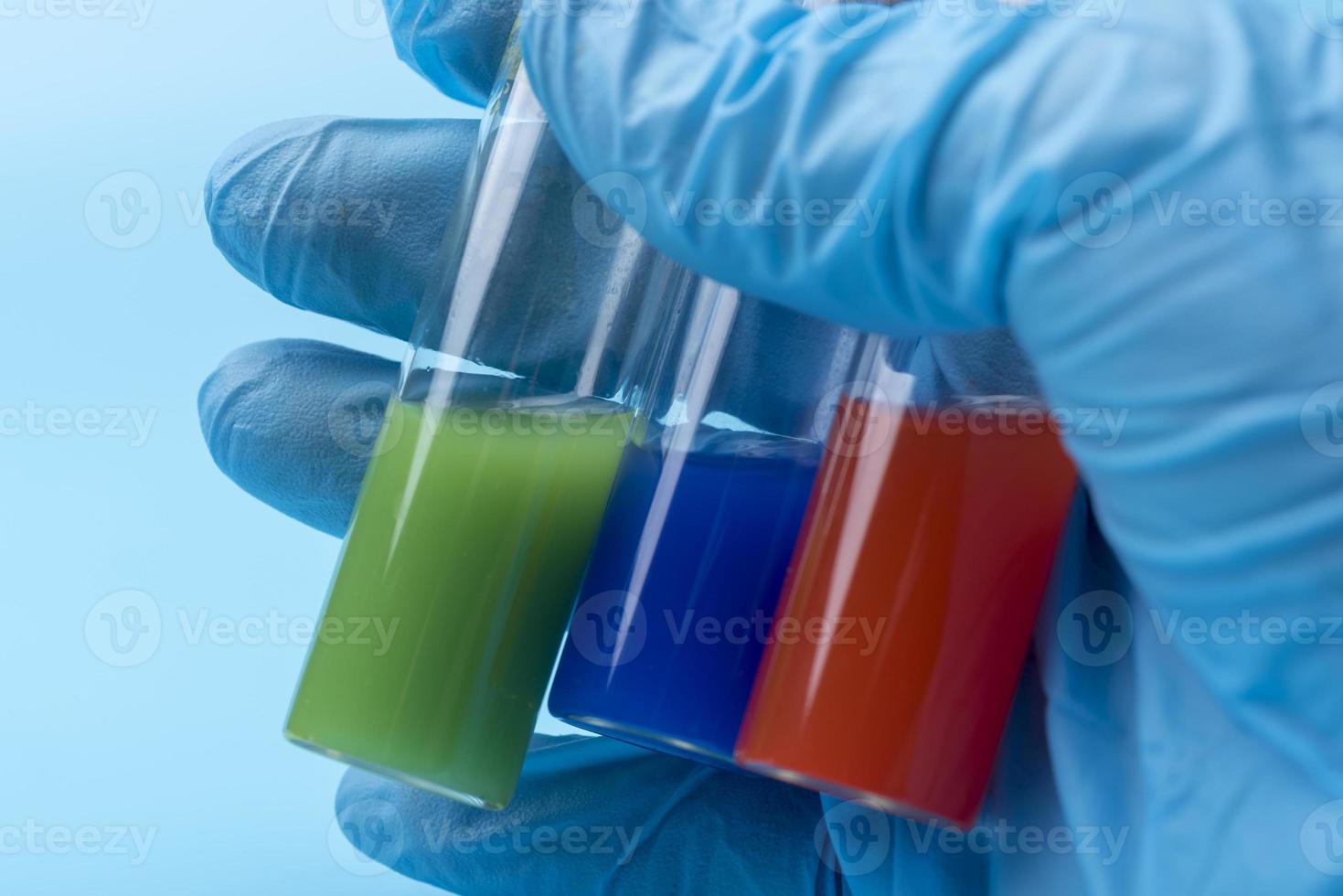 A gloved hand holds three vials of different liquid inside on a blue background. photo