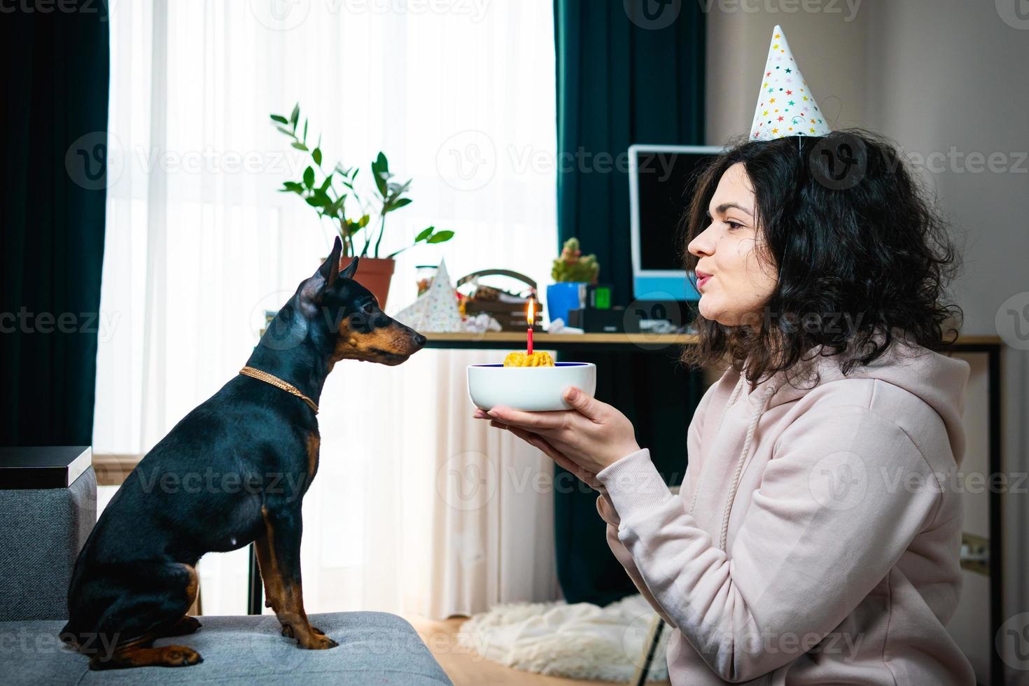 Happy young girl giving homemade cake to her dog, indoors photo