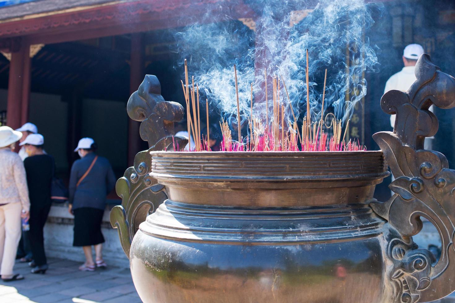 Incense sticks burning in a big pot as temple offering. Vietnam. Incidental people in the background photo