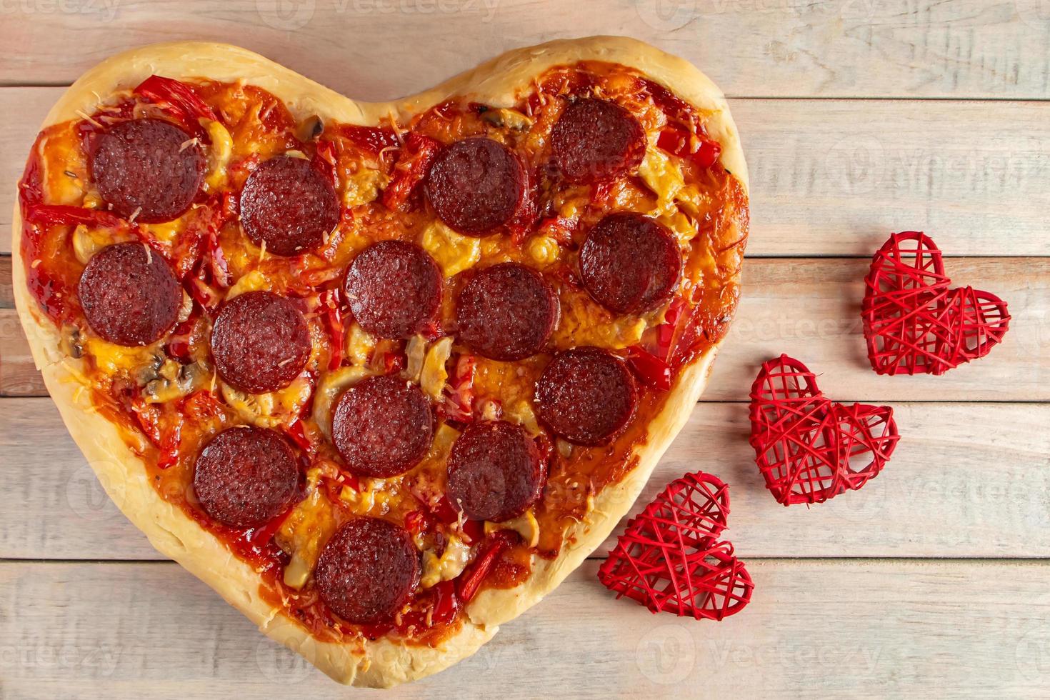Heart shaped pepperoni pizza on wooden background. Valentines day gift. photo