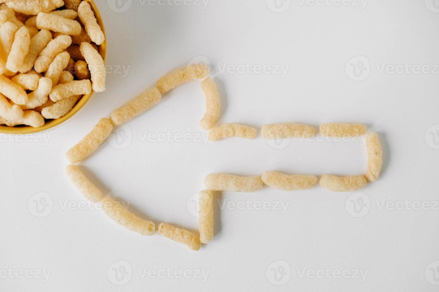 Corn sticks in a yellow bowl scattered in the shape of an pointer on a white background. Top view. Place for your text photo