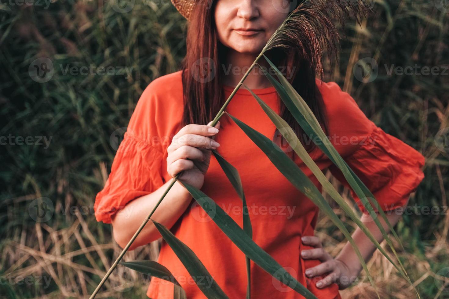 Portrait of a beautiful woman in a straw hat and dressed in red clothes on a background of reeds photo
