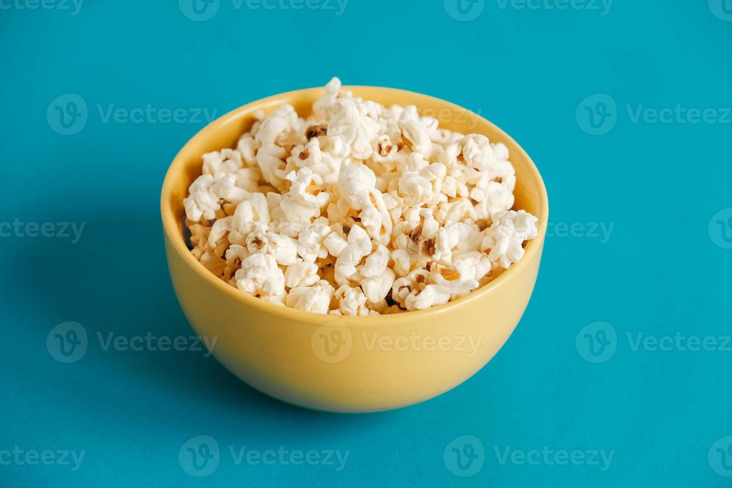 Popcorn in a yellow bowl on a blue background. Copy, empty space for text photo