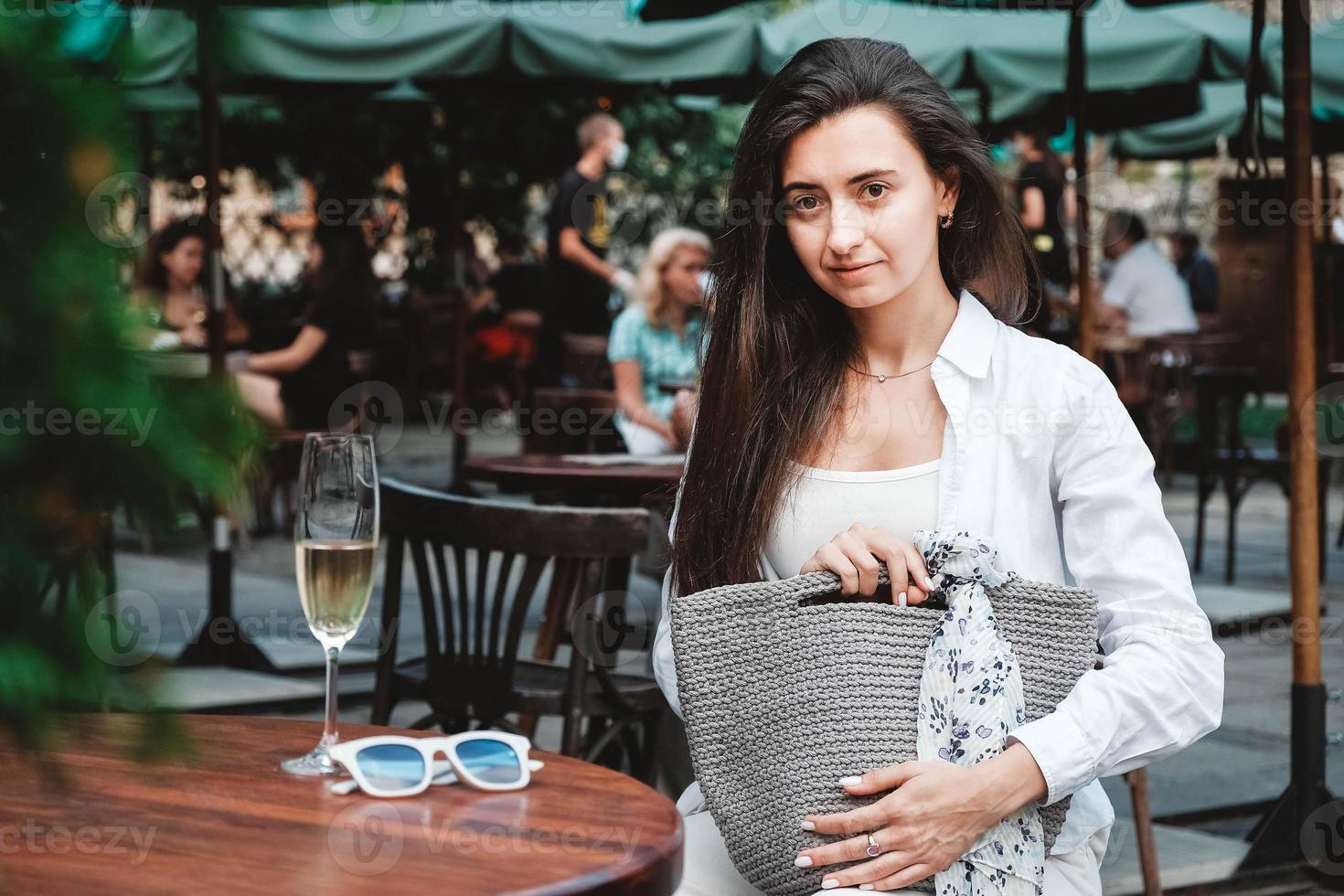 mujer con gafas de sol y ropa blanca, sosteniendo una bolsa de punto sentada en la mesa de un café de la espacio vacío para texto 5272271 Foto de stock