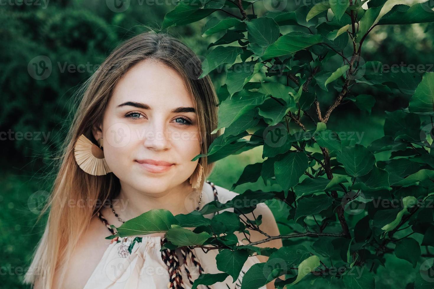 Portrait of a beautiful blonde girl with natural beauty in a green leaves trees. Copy, empty space for text photo