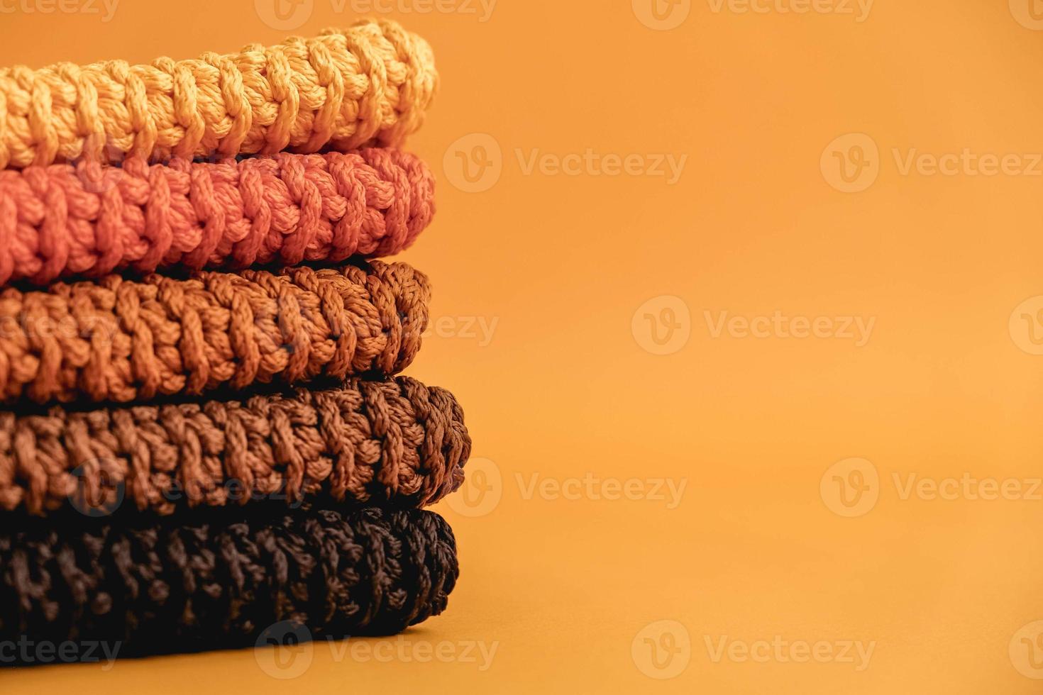Stack of knitted material from threads of yellow, orange, brown colors on a orange background. Copy, empty space for text photo