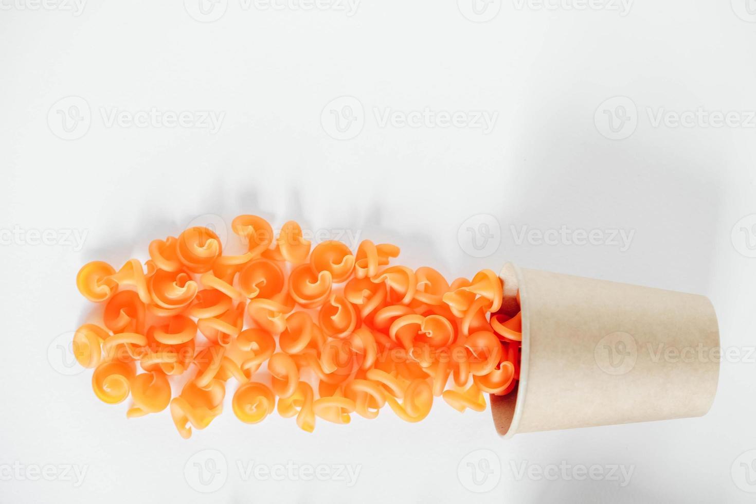 Orange pasta in a disposable kraft paper cup on a white background. Top view. Copy, empty space for text photo