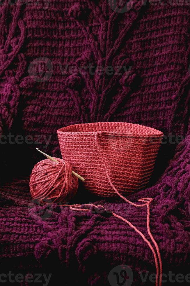 Ball of pink thread with a needle and knitted fabric on a background of purple material. Copy, empty space for text photo