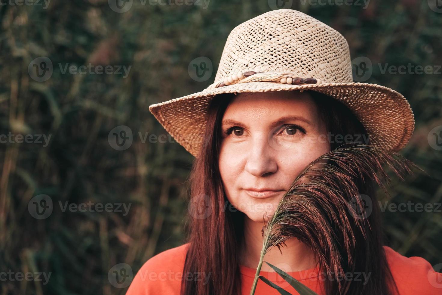 Portrait of a beautiful woman in a straw hat and dressed in red clothes on a background of reeds photo