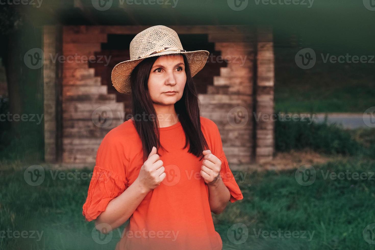 Beautiful woman in a straw hat dressed in red clothes stands on background of a wooden house photo