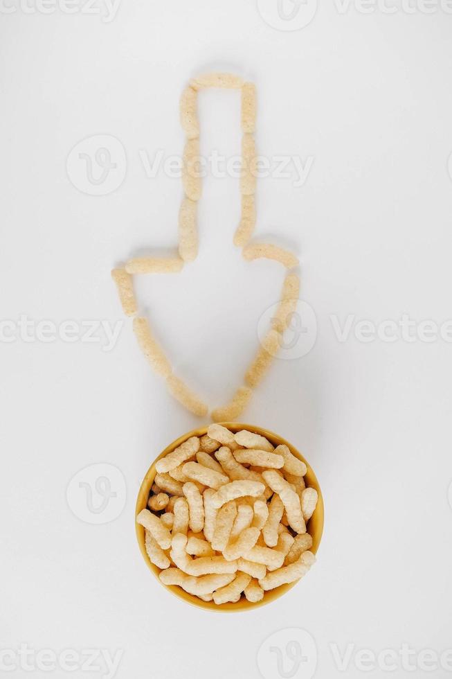 Corn sticks in a yellow bowl scattered in the shape of an pointer on a white background. Top view. Place for your text photo