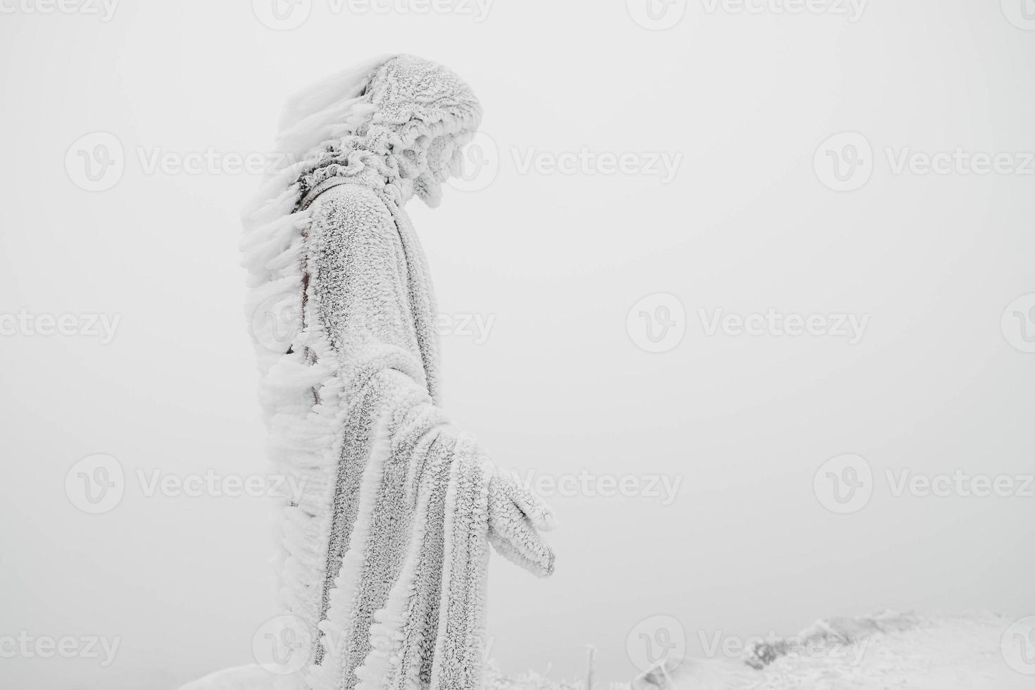 The statue of Jesus is covered with snow and ice on top of mountain photo