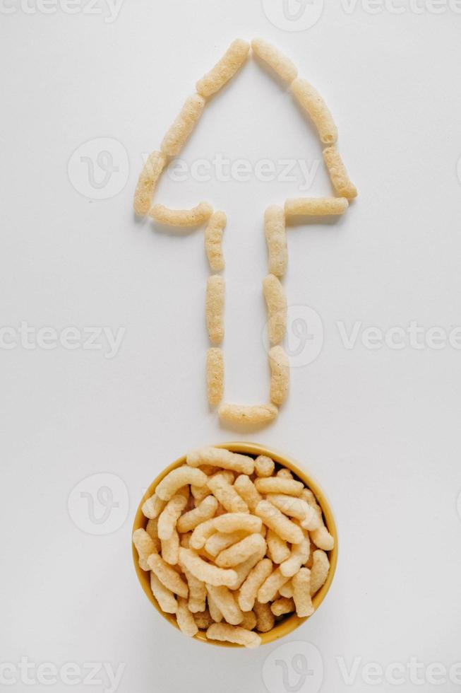 Corn sticks in a yellow bowl scattered in the shape of an pointer on a white background. Top view. Place for your text photo
