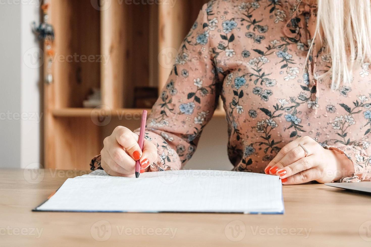 Woman hands with pencil, she is is writing in her notebook sitting at the table with book shelf background. Copy, empty space for text photo