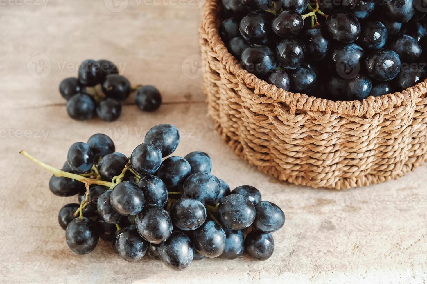 Bunch of black grapes in a round wicker basket on a old wooden table. Copy, empty space for text photo