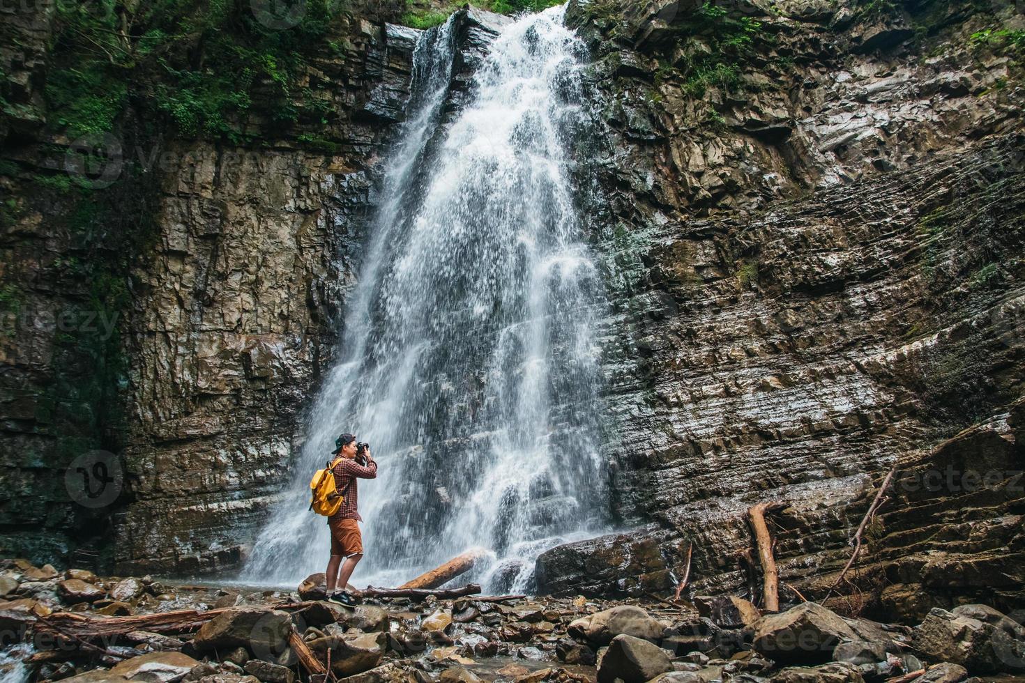 Hombre viajero con una mochila amarilla de pie sobre el fondo de una cascada hace un paisaje fotográfico foto