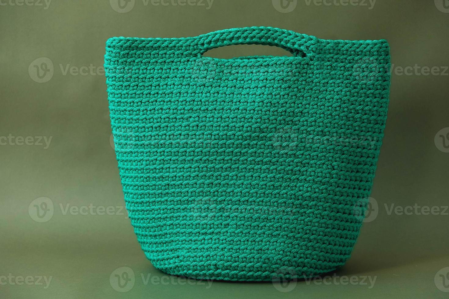 Stylish woman's knitted green bag on green background. Copy, empty space for text photo