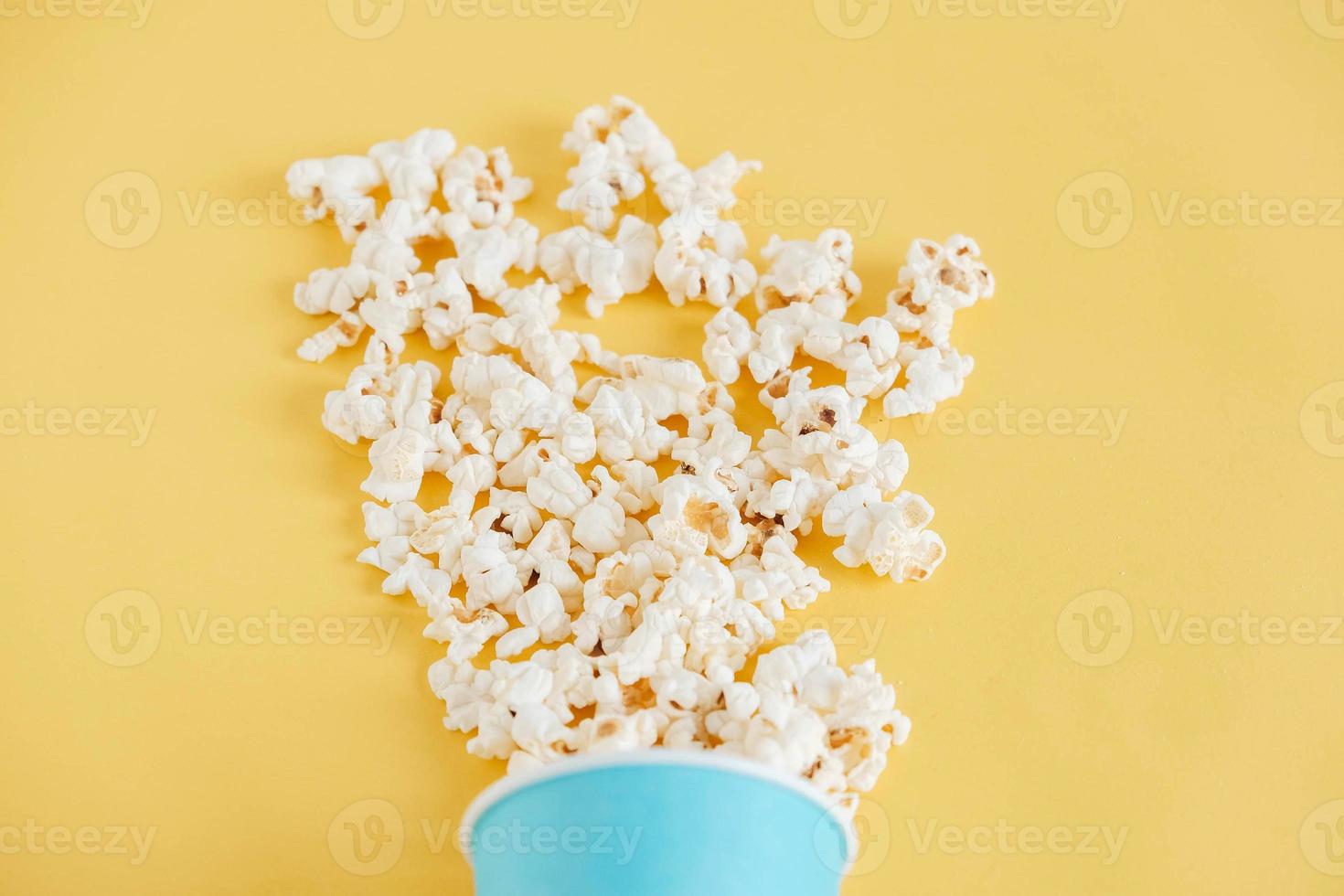 Popcorn in a blue paper cup scattered on a yellow background. Minimalist concept. Top view. Copy, empty space for text photo